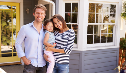 Married couple holding child standing in front of home.